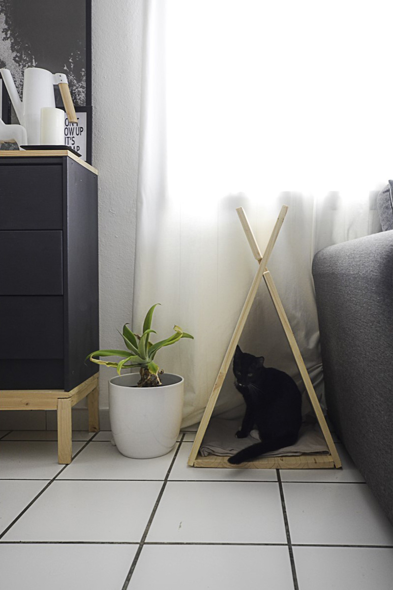 Tipi pour chat posé en bout de canapé avec un chat noir à l'intérieur